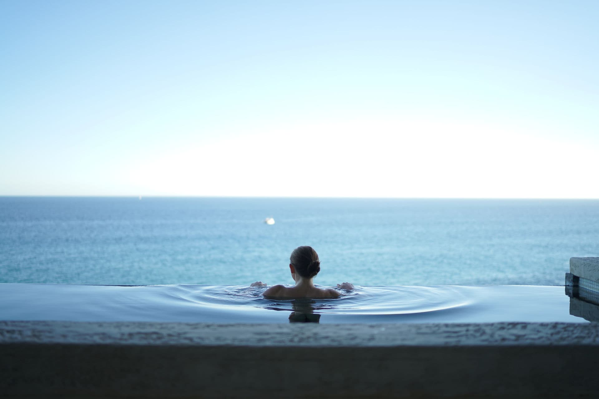Woman relaxing in infinity pool with ocean horizon — luxury lifestyle